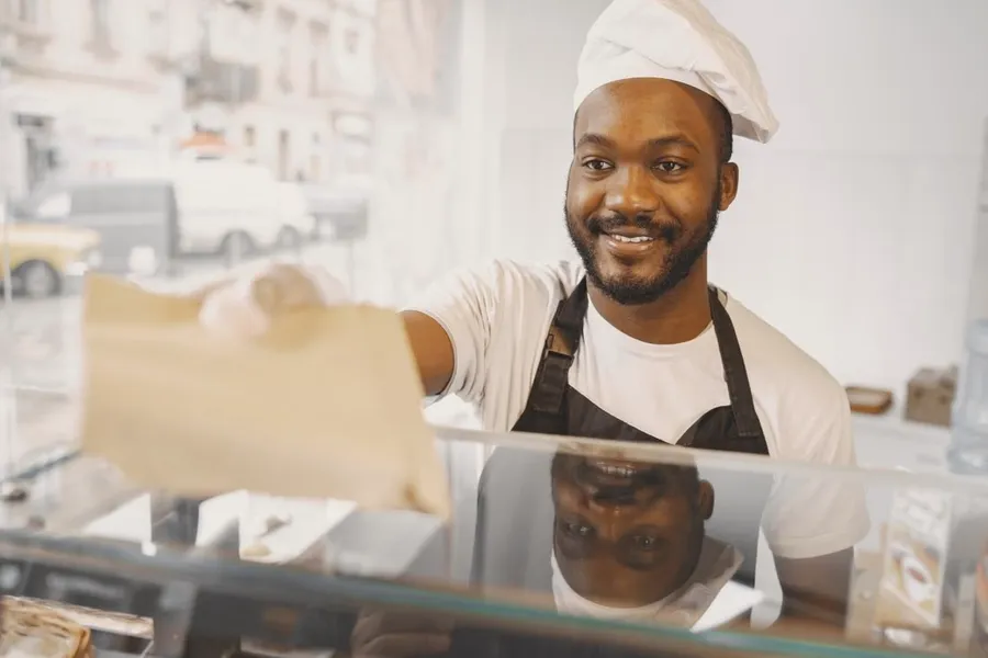 A smiling baker handing an order across the counter